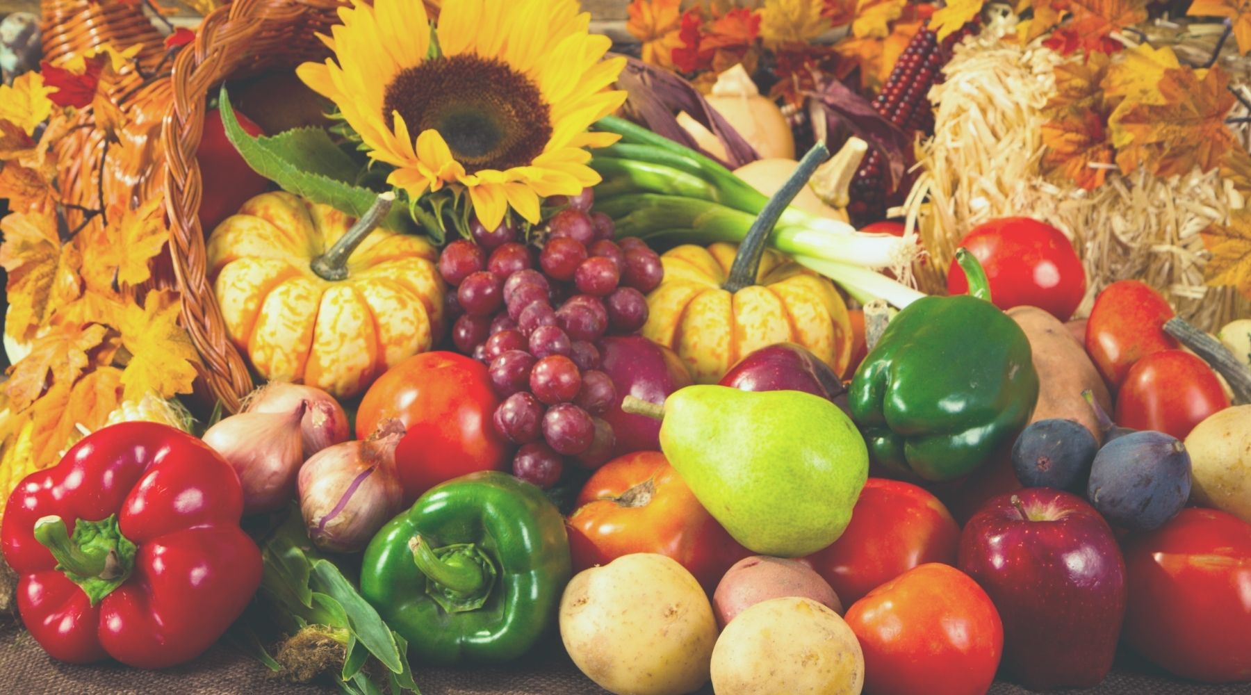 Autumn harvest with seasonal fruits like apples, pears, grapes, pumpkins, and bell peppers, surrounded by fall leaves and a sunflower for a festive touch.