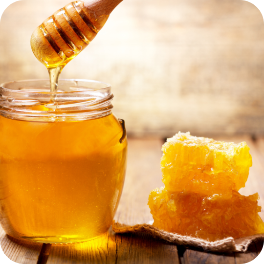 Fresh honey dripping from a dipper into a jar with honeycomb pieces on a rustic background.