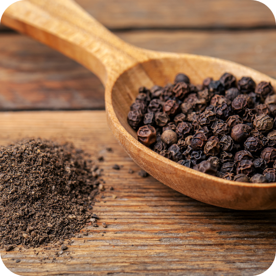 Whole black peppercorns in a wooden spoon and ground pepper on a rustic wooden surface.